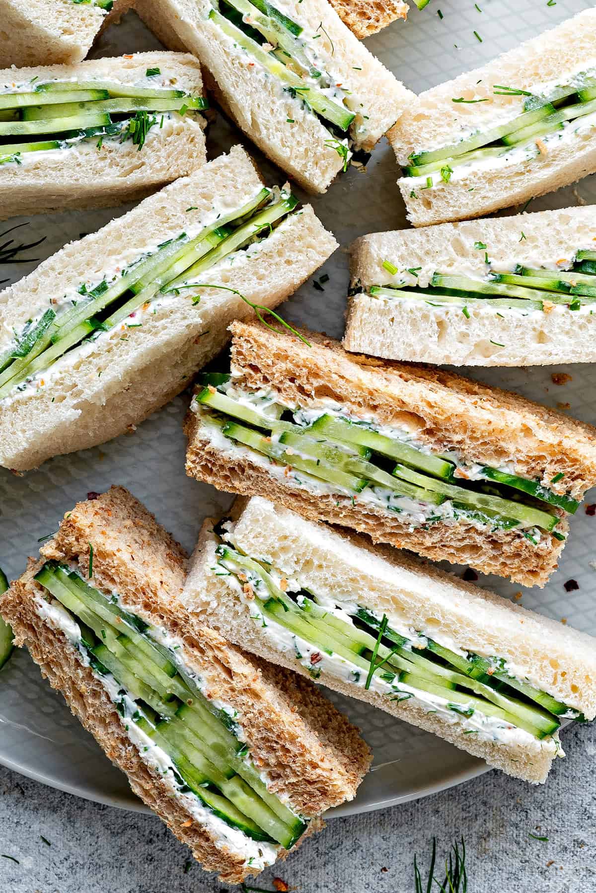 Close up view of a half dozen cream cheese cucumber sandwiches, all on their sides to show the middles to camera.