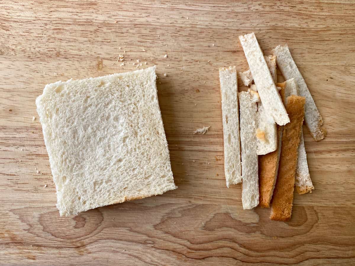 A piece of white bread on a cutting board with the crusts cut off.