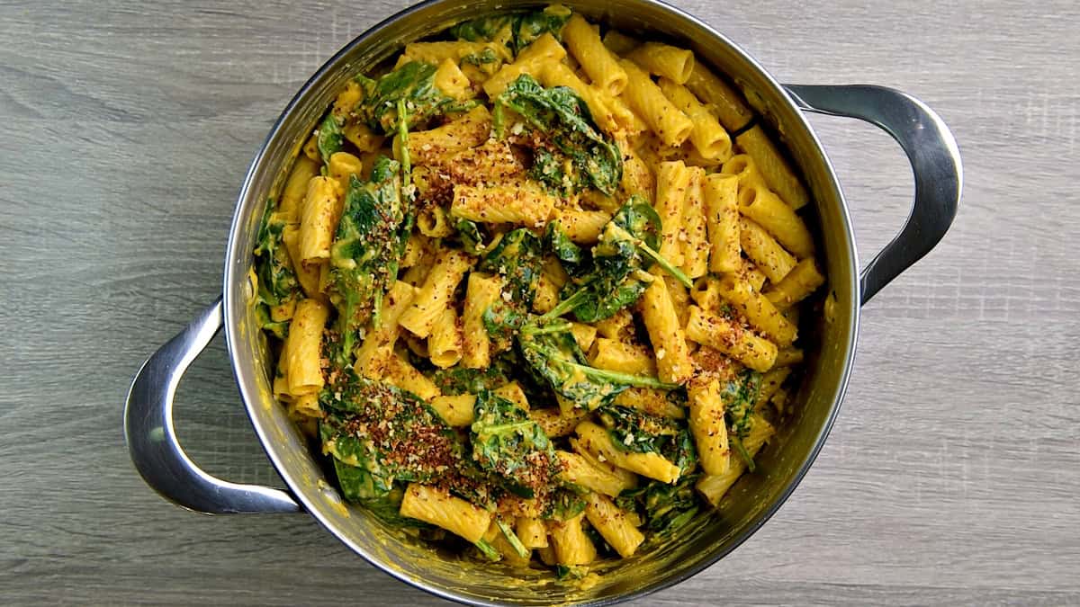 A pot full of pumpkin pasta with spinach, herbs, and toasted panko breadcrumbs sprinkled on top. 