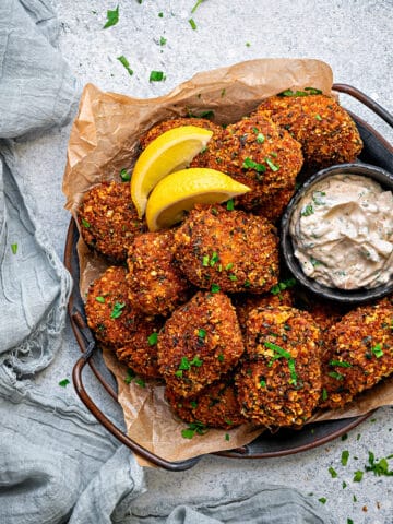 A dish full of fish nuggets served alongside lemon wedges and a sauce in a bowl.