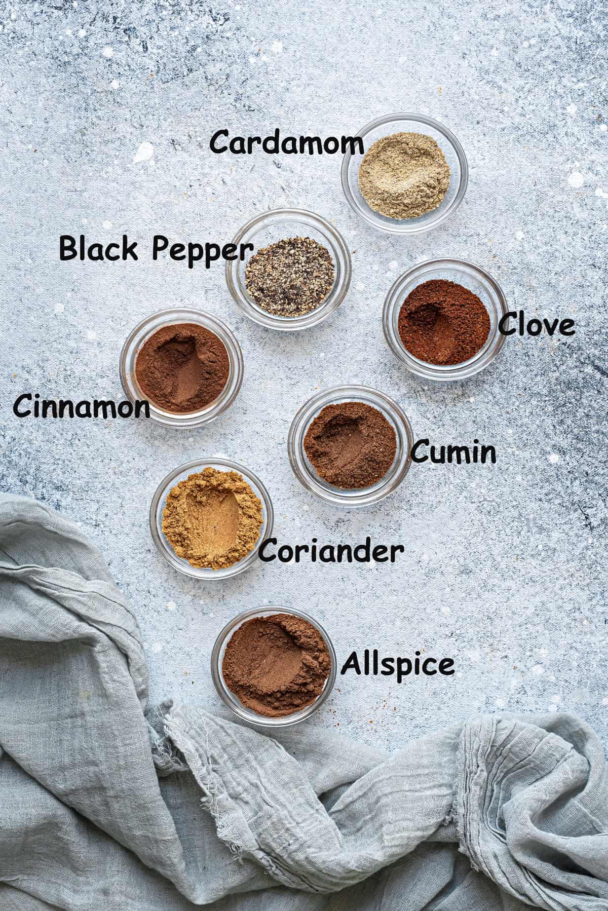Individual mini bowls of ground cardamom, black pepper, clove, cinnamon, cumin, coriander, and allspice.