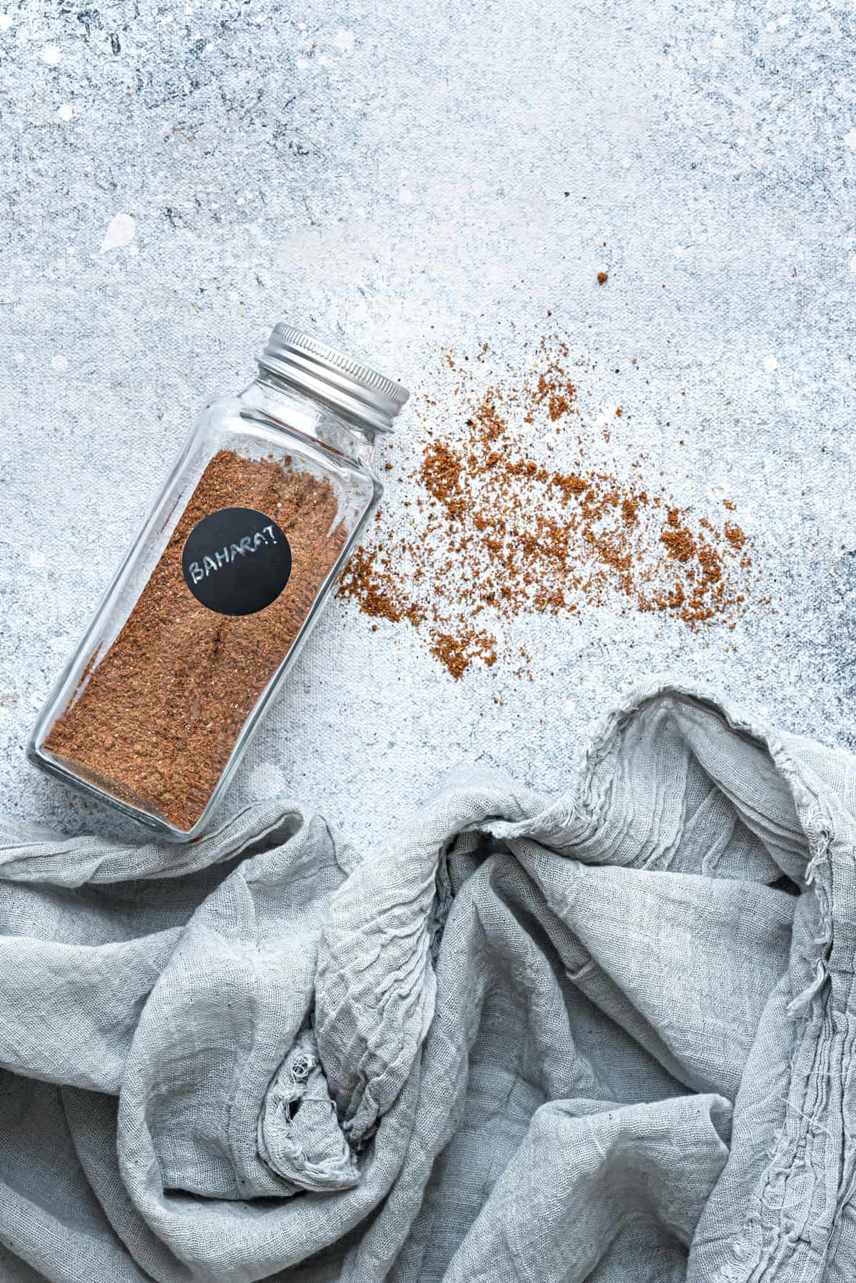 A jar of homemade baharat blend with some spice sprinkled out on to the surface.