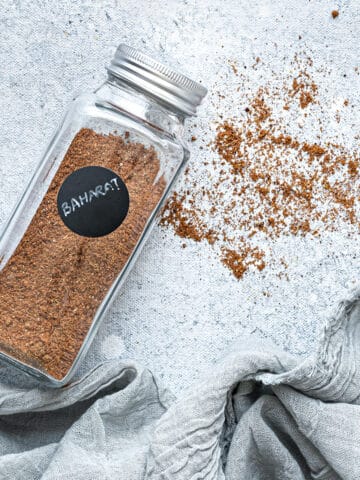 A jar of homemade baharat spice with some of the spice sprinkled out on the counter.
