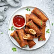 A plate full of chinese style chicken bread pockets with on bread roll cut open to show the filling. A dipping sauce next to them.