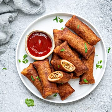 A plate full of chinese style chicken bread pockets with on bread roll cut open to show the filling. A dipping sauce next to them.
