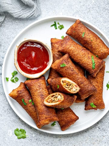 A plate full of chinese style chicken bread pockets with on bread roll cut open to show the filling. A dipping sauce next to them.