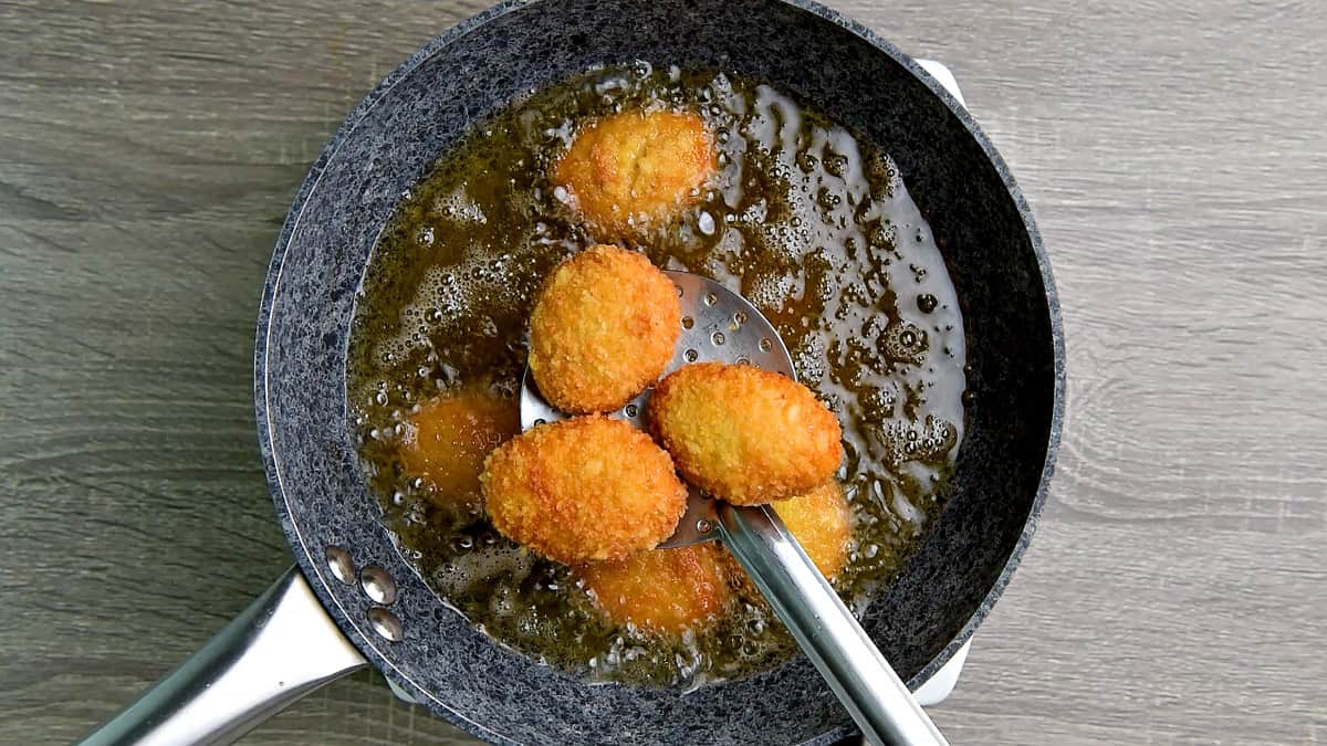 Removing fried nuggets from the oil with a slotted spoon.