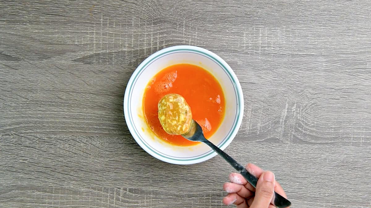Dredging the nugget through beaten egg in bowl.