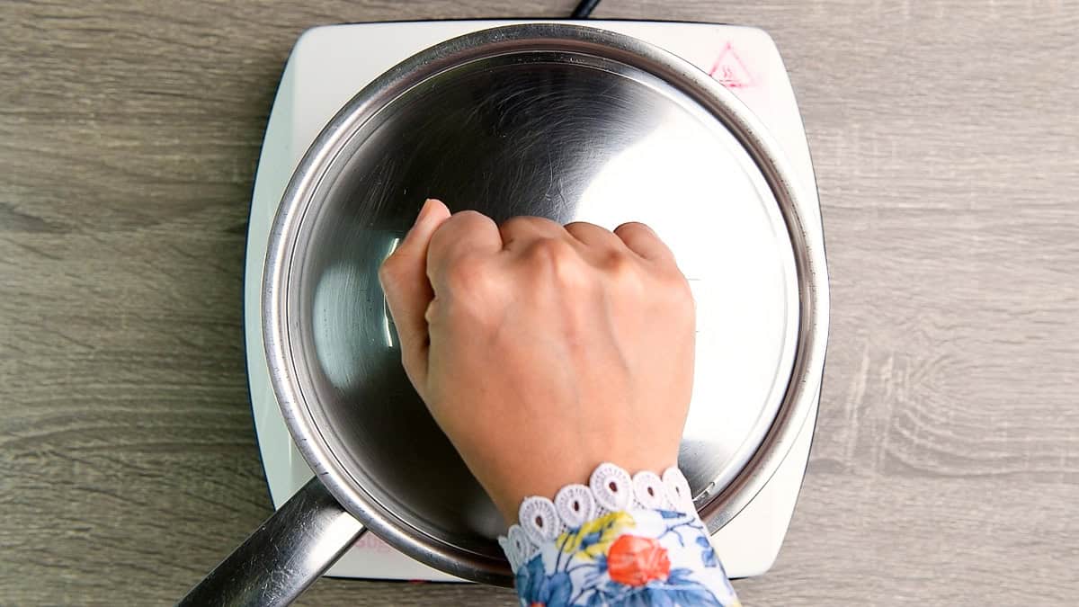 A hand covering the pot of simple syrup to steep. 