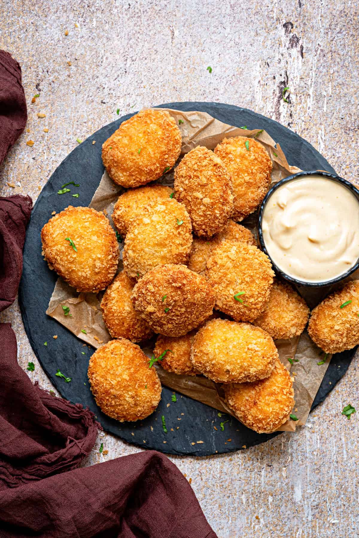 A plate of crispy chicken nuggets a serving slate with a ramekin of sauce on the side.