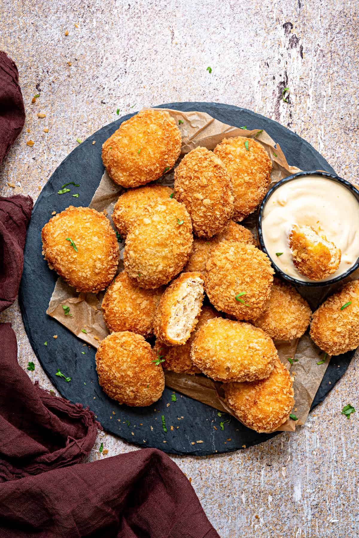A plate full of homemade fried chicken nuggets with one cut open piece in a dipping sauce.