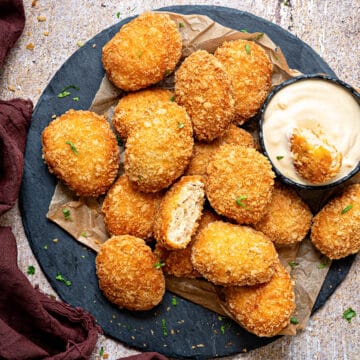 A plate full of homemade fried chicken nuggets with one cut open bite in a dipping sauce.