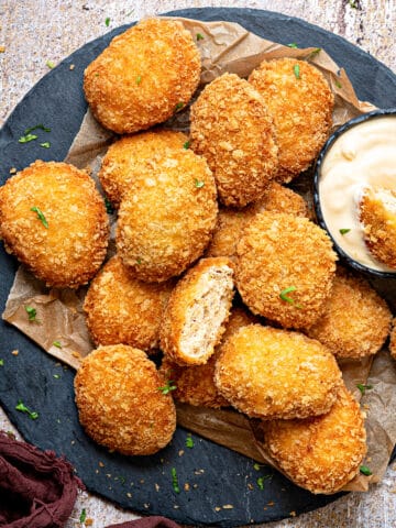 A plate full of homemade fried chicken nuggets with one cut open bite in a dipping sauce.