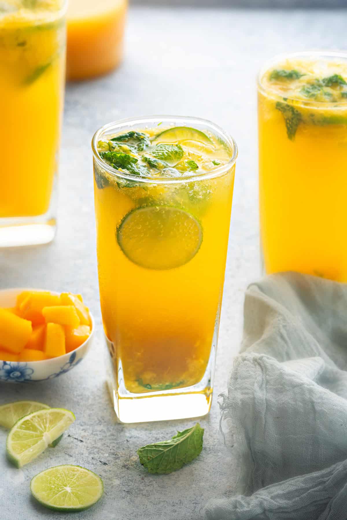 Three mango mojito mocktails garnished with lime and mint.