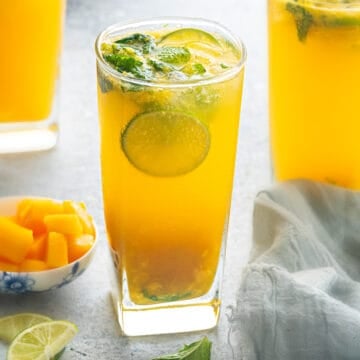 Three mango mojito mocktails garnished with lime and mint.