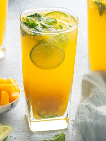 Three mango mojito mocktails garnished with lime and mint.