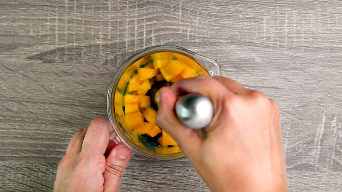 Muddling mango chunks with lime and mint leaves in the pitcher.