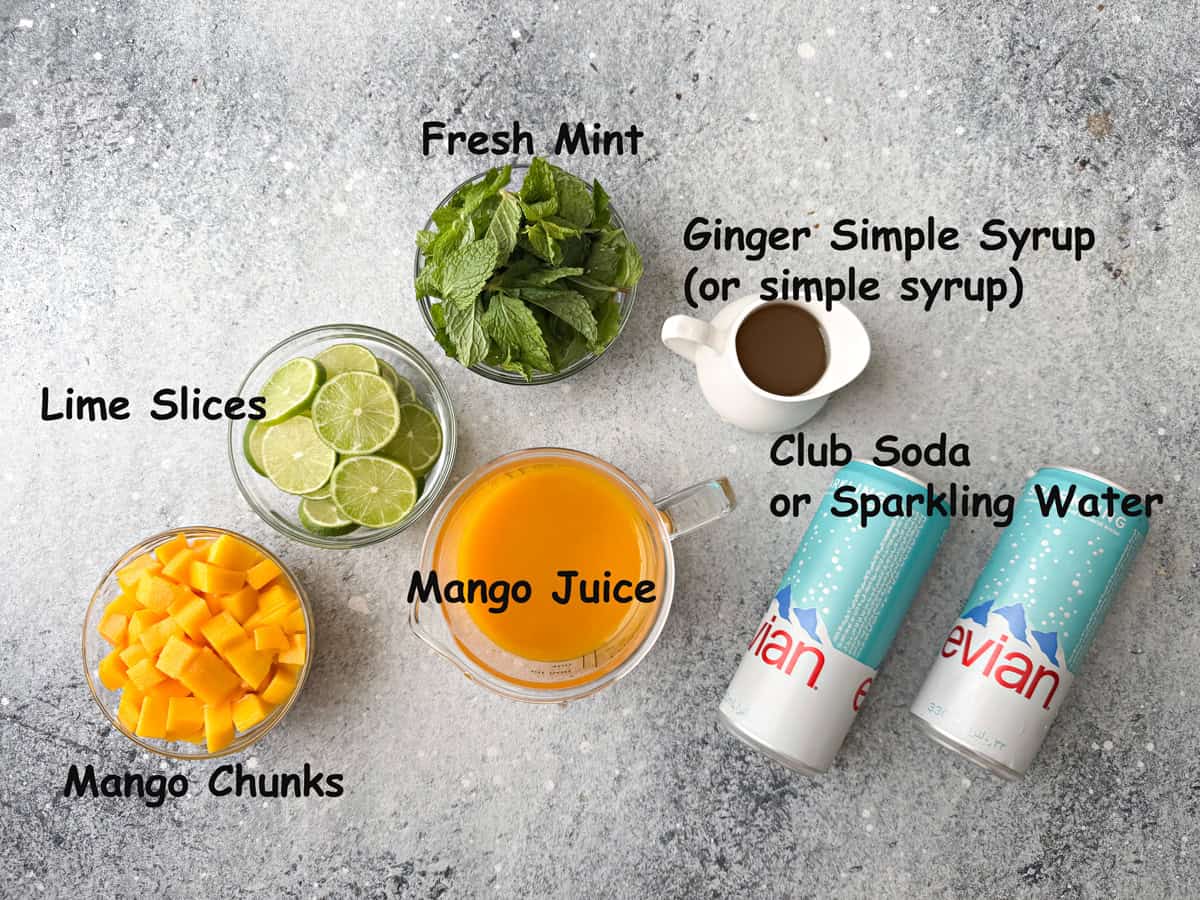 Recipe ingredients - mango juice, ginger simple syrup, fresh mint, lime slices, and mango chunks in individual glass bowls and sparkling water cans.