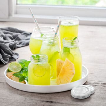 Several jars and glasses full of pineapple mojito mocktails on a circular serving platter.
