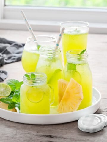 Several jars and glasses full of pineapple mojito mocktails on a circular serving platter.