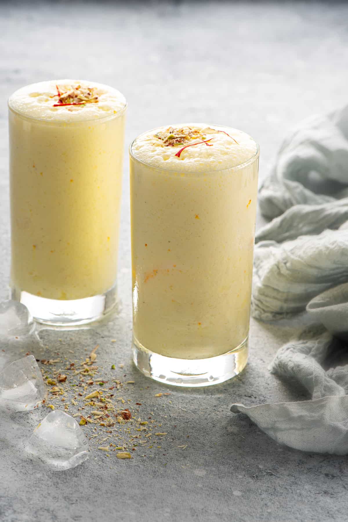 Two glasses of Punjabi sweet lassi topped with nuts and saffron strands.