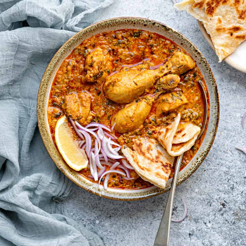 Grey earthen bowl with methi chicken curry.