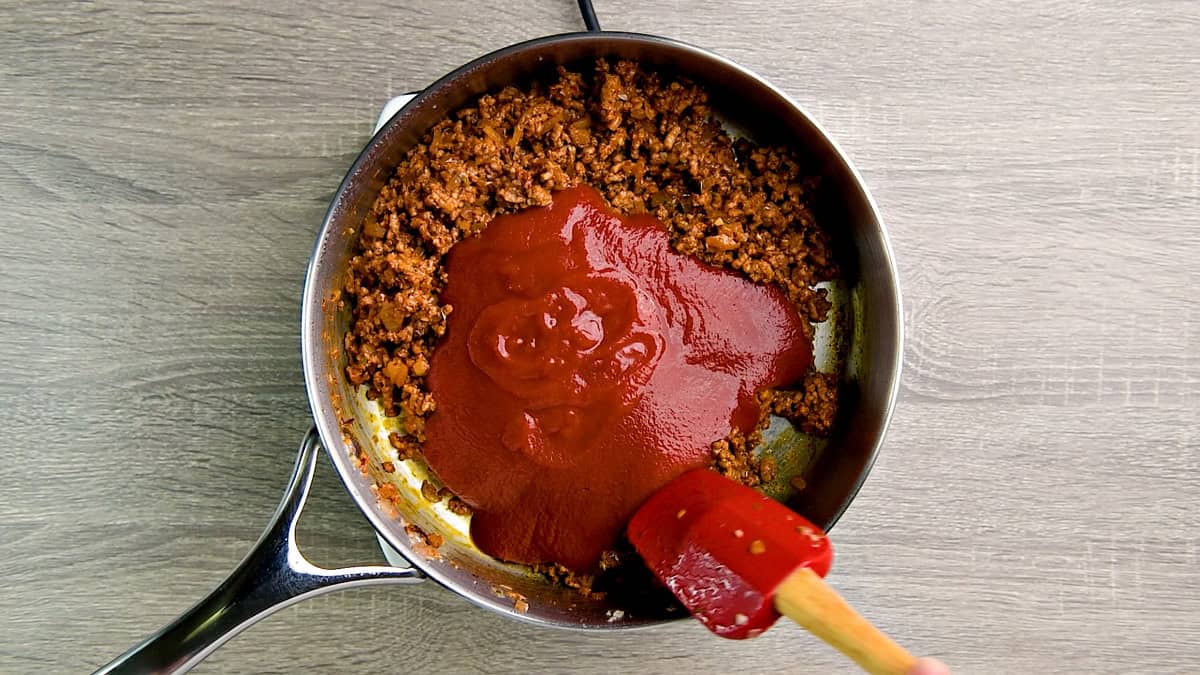 Tomato sauce added to cooked ground beef in a large deep skillet.