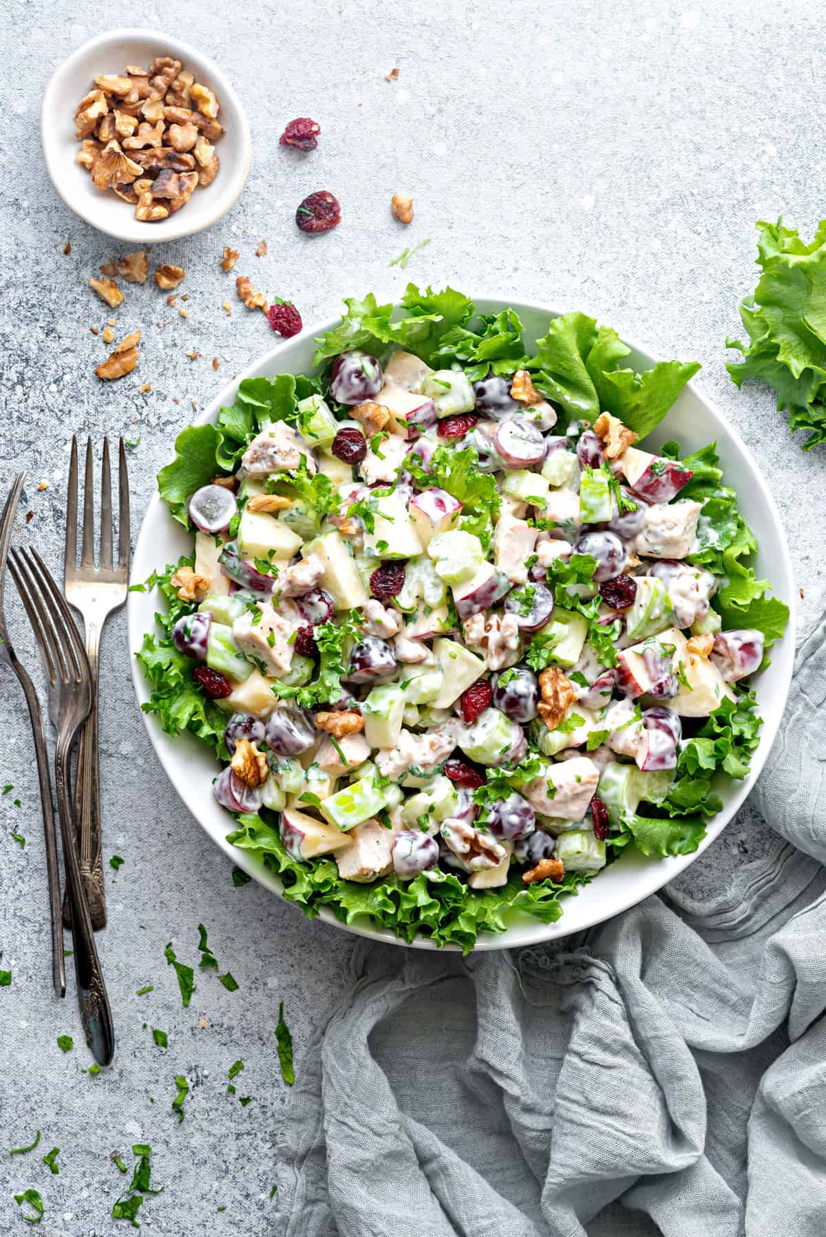 Top-down view of Waldorf Salad with Chicken in a large serving bowl on a bed of lettuce, a small bowl of walnuts, and some forks.