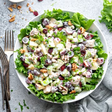 Waldorf Salad with Chicken in a large serving bowl on a bed of lettuce, a small bowl of walnuts, and some forks