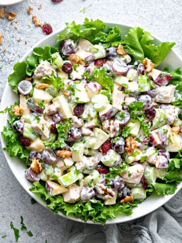 Waldorf Salad with Chicken in a large serving bowl on a bed of lettuce, a small bowl of walnuts, and some forks