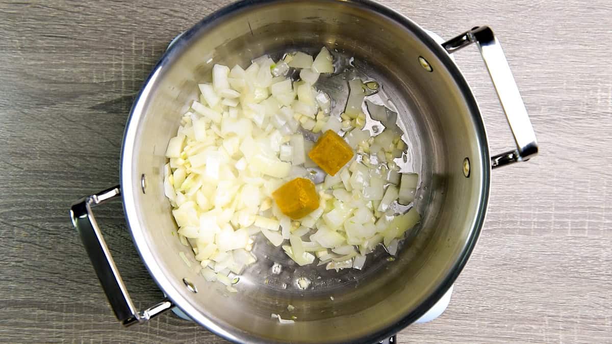 Two cubes of yellow curry paste added to the pot with sautéed onion and garlic.