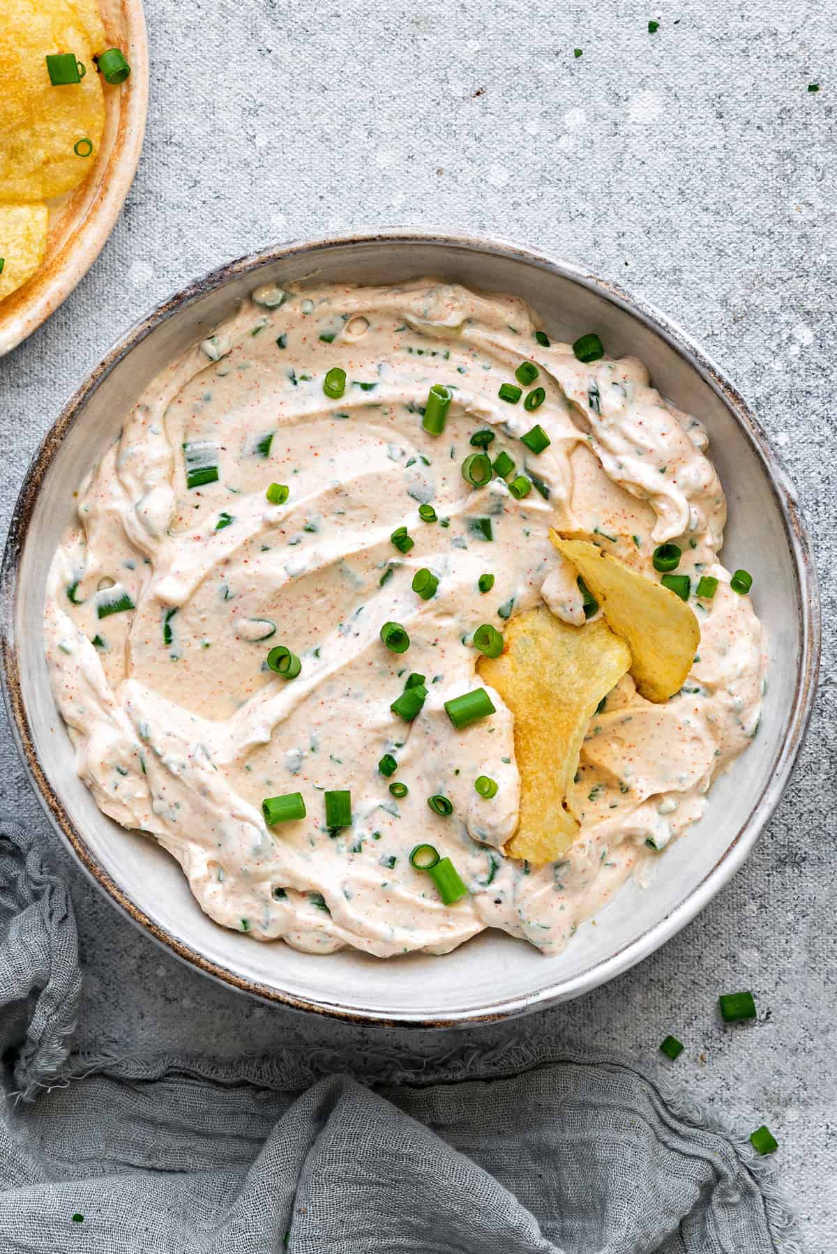 Top-down view of Cream Cheese Dip in a bowl, topped with green onions and crispy chips dipped into it.