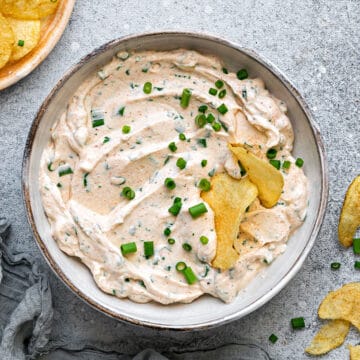 Cream Cheese Dip in a bowl, topped with green onions and crispy chips dipped into it.