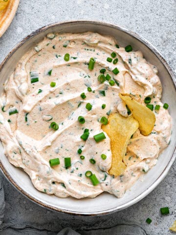 Cream Cheese Dip in a bowl, topped with green onions and crispy chips dipped into it.