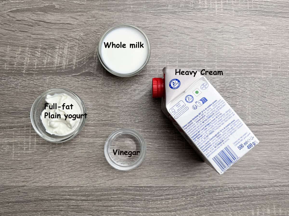 Top-down view of ingredients for homemade sour cream: Full plain yogurt, vinegar, heavy cream, and whole milk.