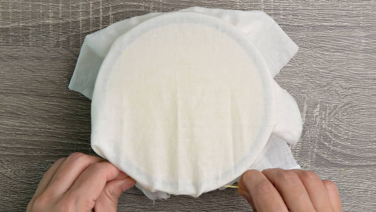 Hands covering the Sour cream starter with cheesecloth in the glass container to let it ferment.