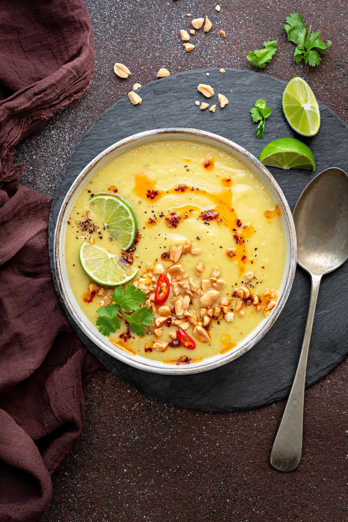 Top-down view of parsnip soup with apple topped with lime wedges, nuts, chili oil and cilantro.