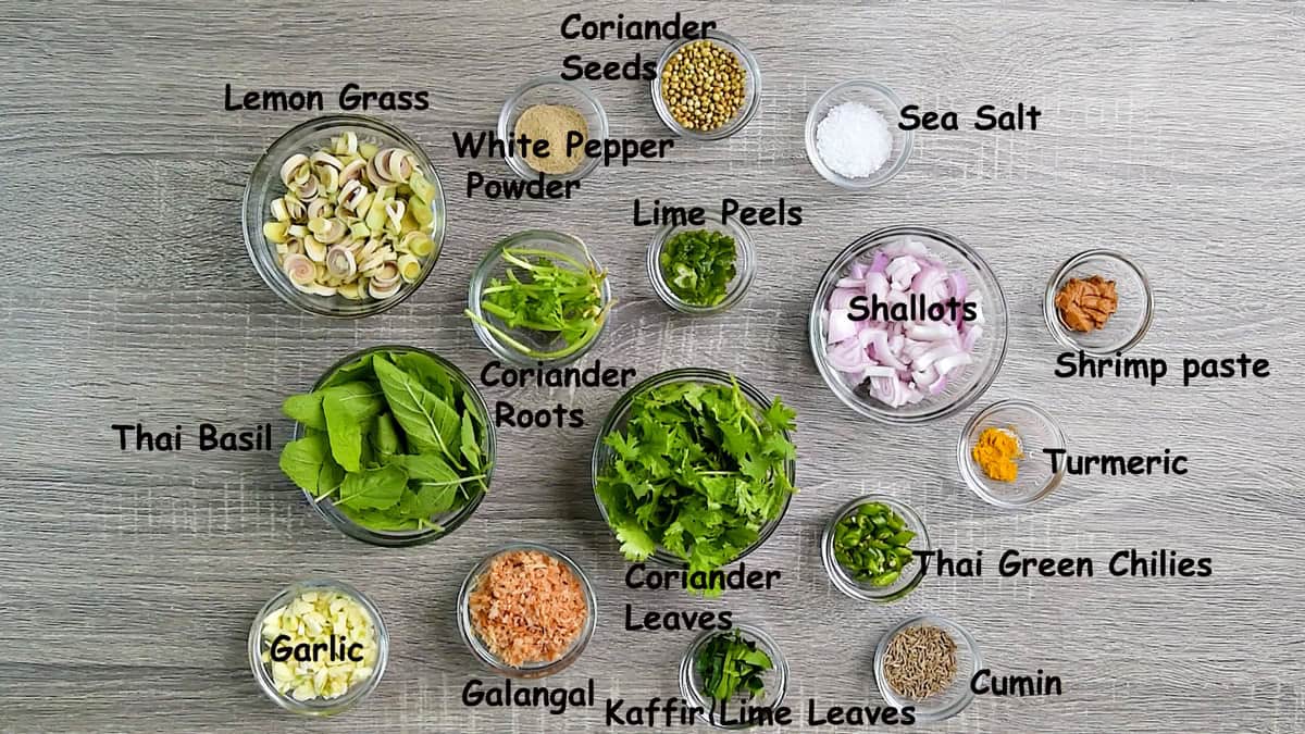Top-down view of Thai green curry paste ingredients in individual glass bowls laid on a gray table.