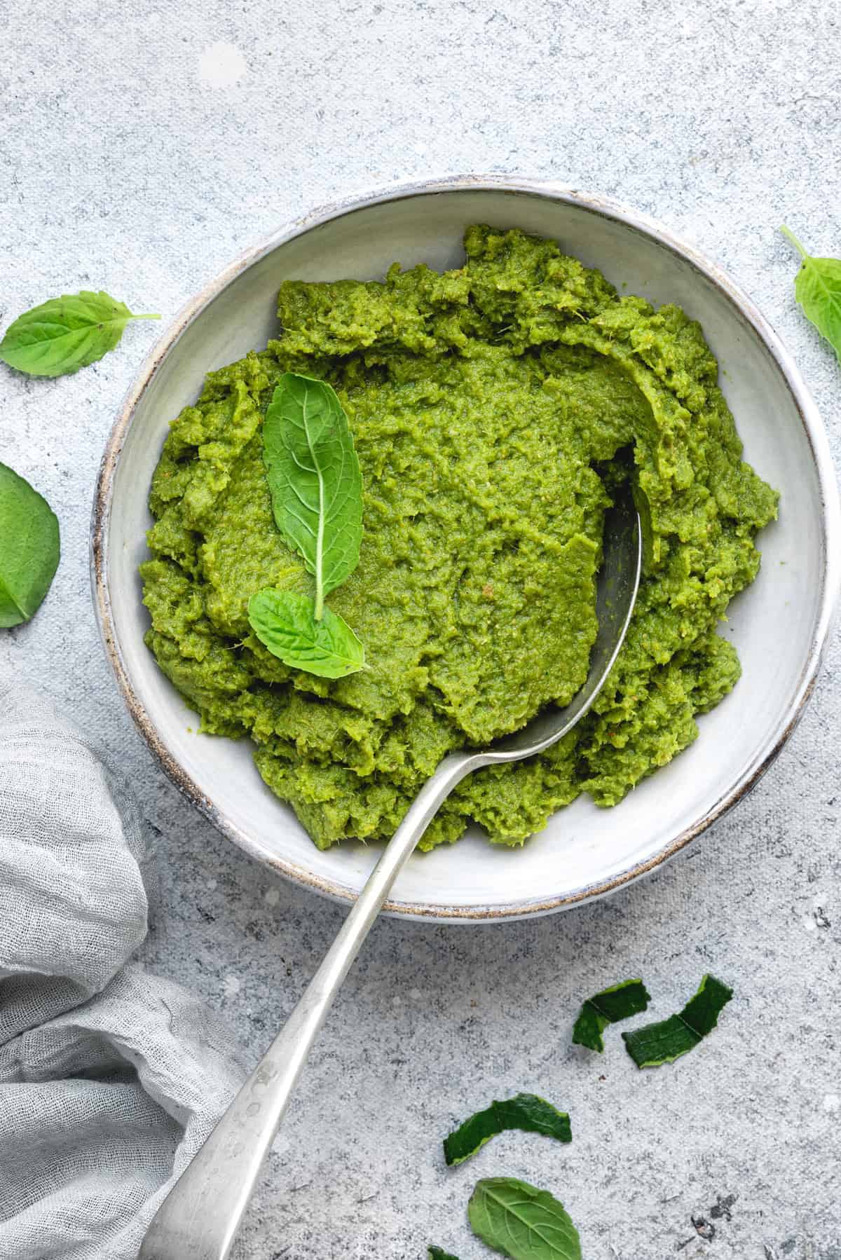 Top-down view of green Thai curry paste in a bowl with Thai basil leaves, and a spoon ladling the curry paste.
