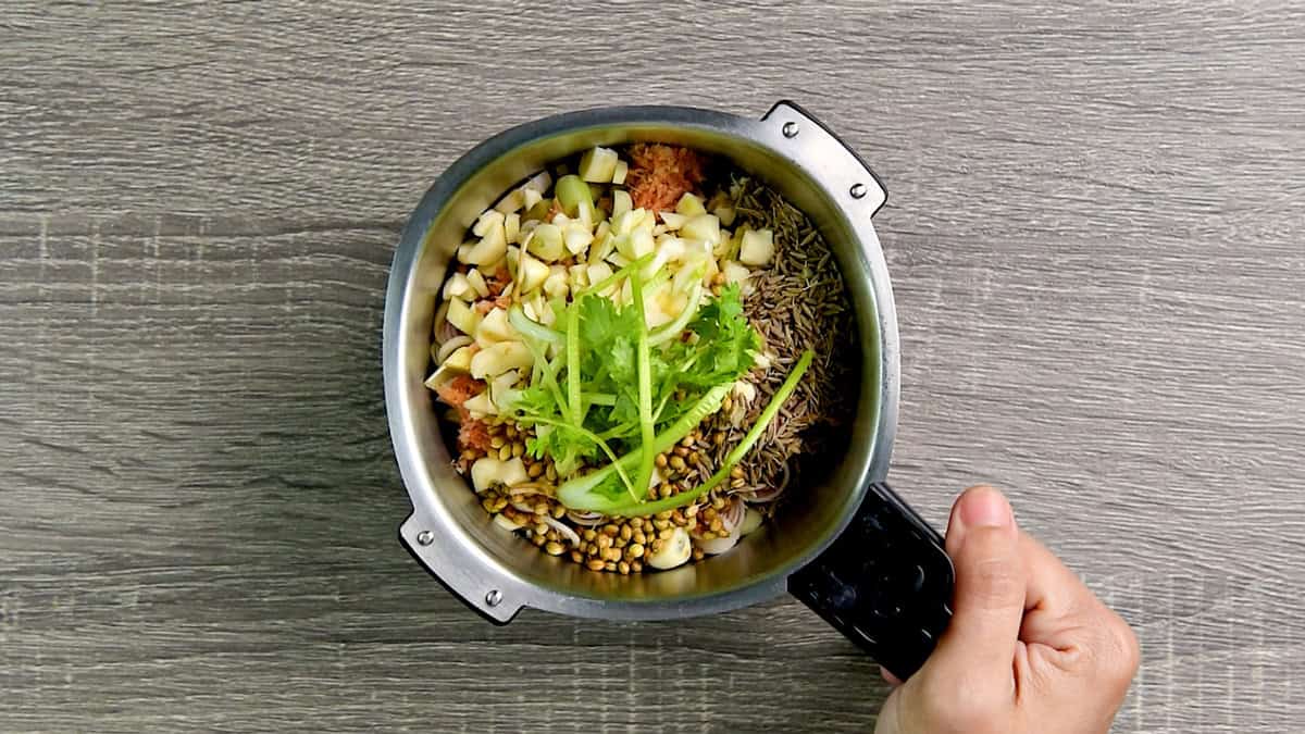 Top-down view of green curry paste ingredients in a blender with the lid off, which include lemon grass, coriander seeds, cumin, garlic, and galangal.