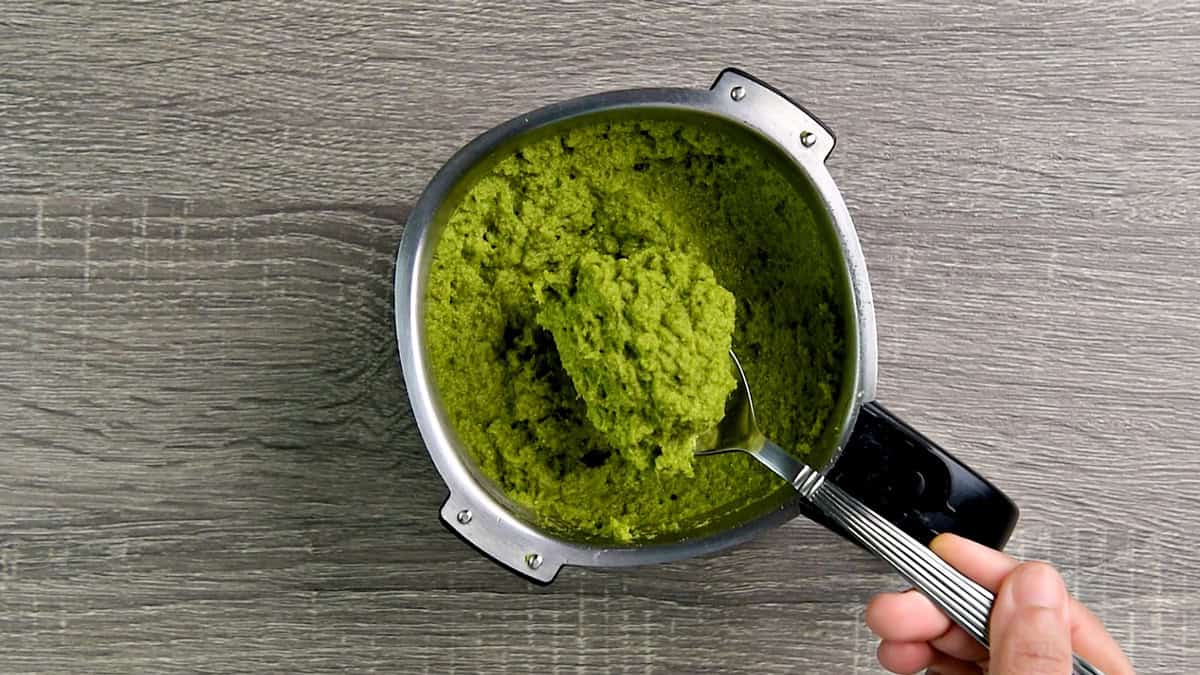 Top-down view of green Thai curry paste ingredients in a blender that has been blended until smooth and ready to serve, which includes shallots, green Thai chilies, kaffir limes, turmeric, and more.