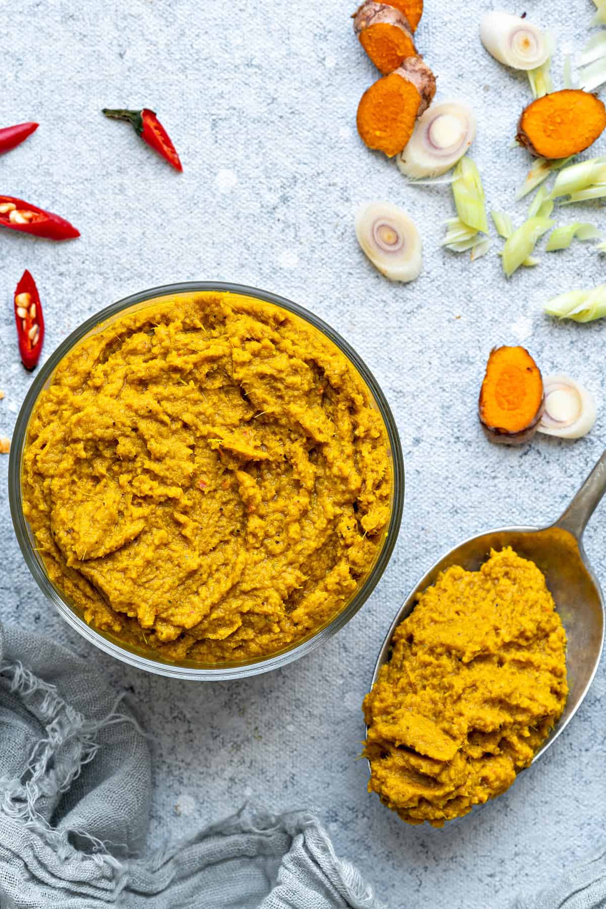 Top-down view of Thai Yellow curry paste in a bowl that is ready to be served, surrounded by bird's eye chilies, turmeric, and lemongrass.