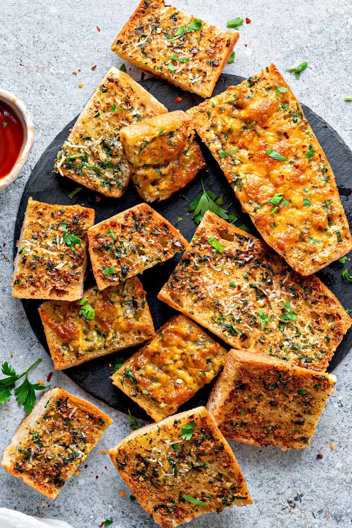 Top-down view of air fryer garlic bread on a plate topped with parsley and shredded parmesan. 