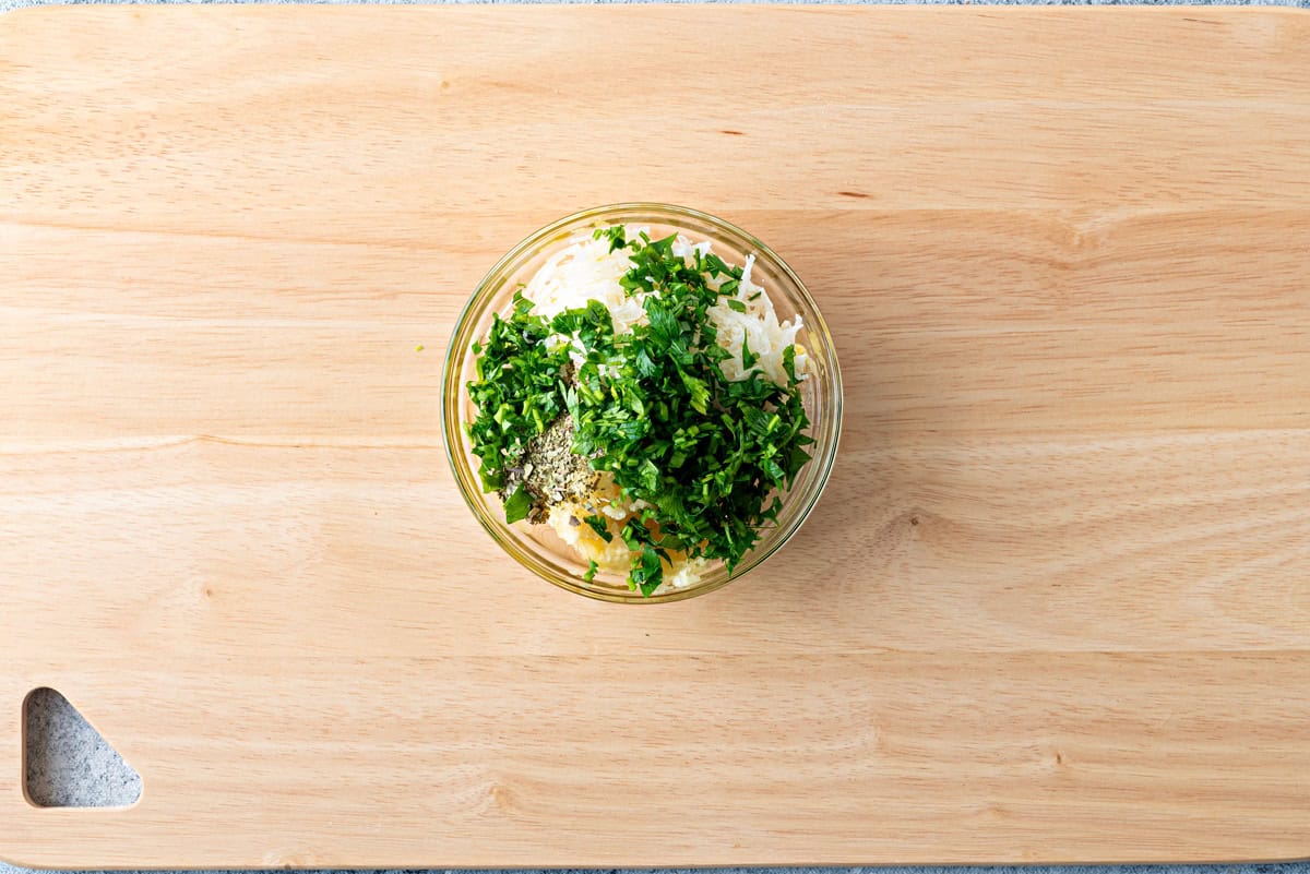 Top-down view of garlic butter ingredients in bowl that includes parsley, dried basil, dried oregano, red pepper flakes, and garlic.