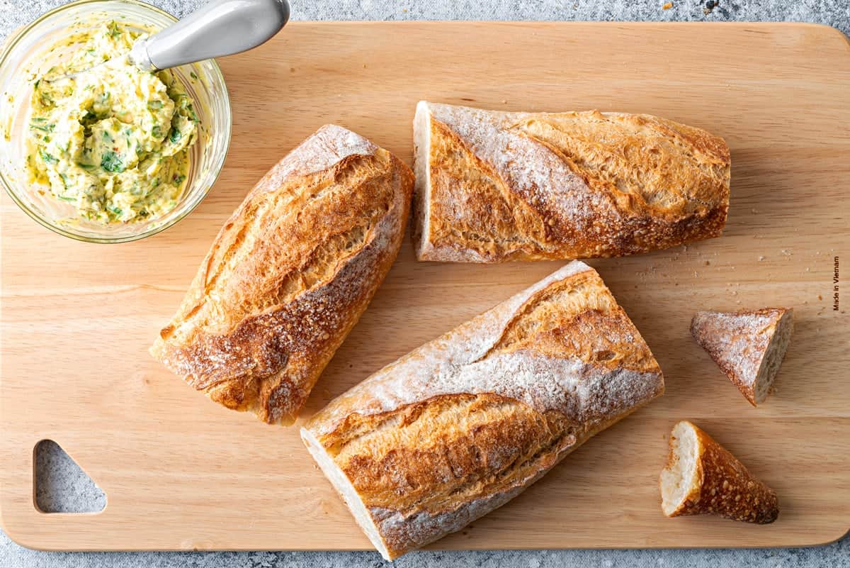 Top-down view of garlic butter mixture and baguette that has been cut into 3rds on a cutting board.