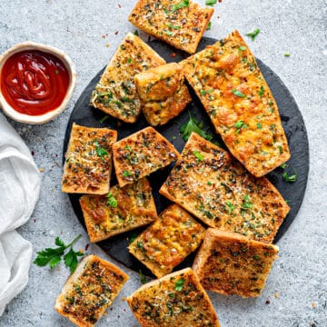 Top-down view of air fryer garlic bread on a plate topped with parsley and shredded parmesan.