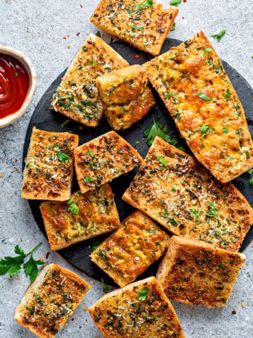 Top-down view of air fryer garlic bread on a plate topped with parsley and shredded parmesan.