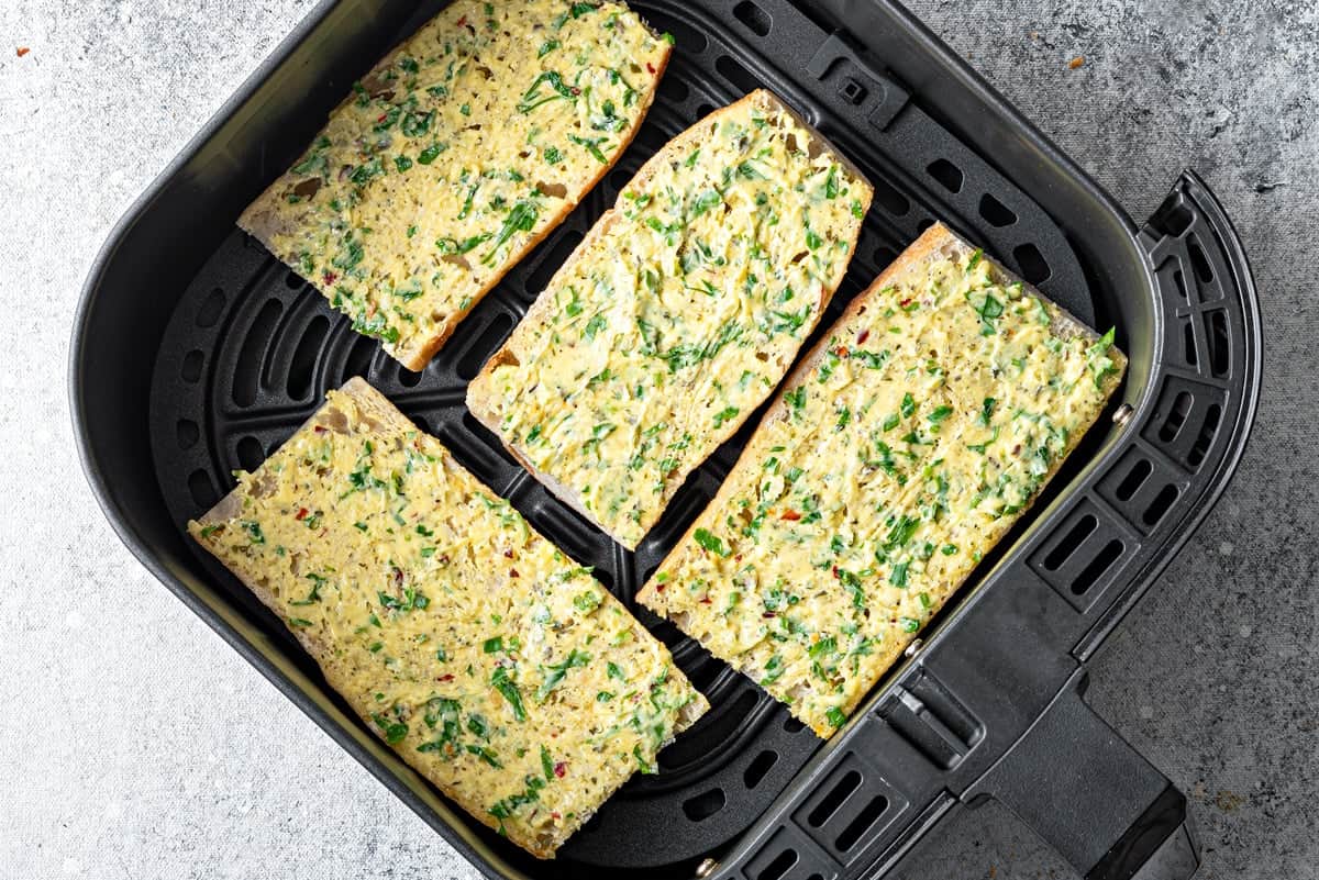 Top-down view of prepared garlic bread in an air fryer that is evenly spaced and not stacked on top of each other.