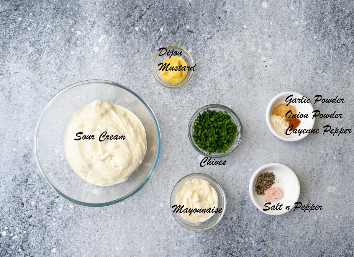 Top-down view of the recipe ingredients placed in an individual glass bowl: it includes sour cream, dijon mustard, chives, mayonnaise, spices, salt and pepper.