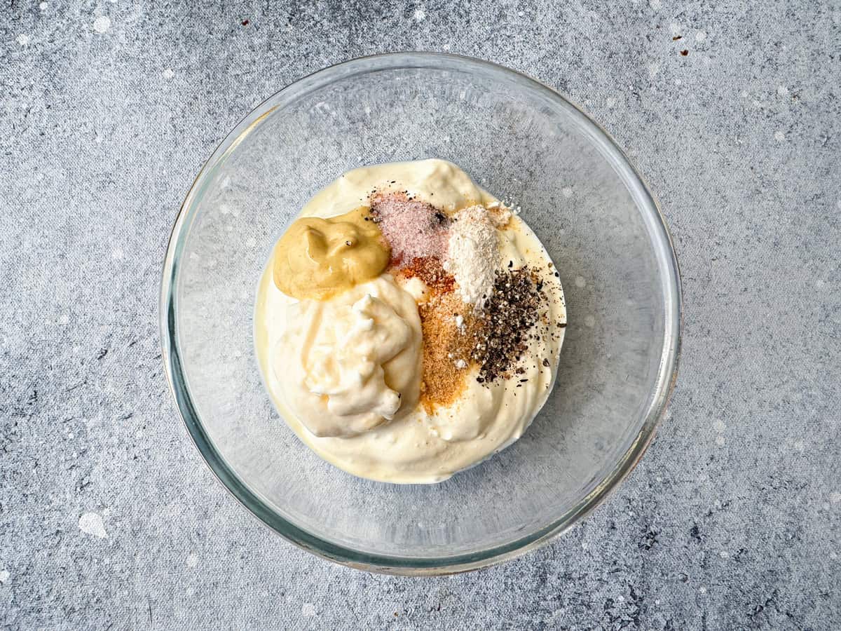 A medium glass bowl with sour cream, mayonnaise, dijon and seasonings.